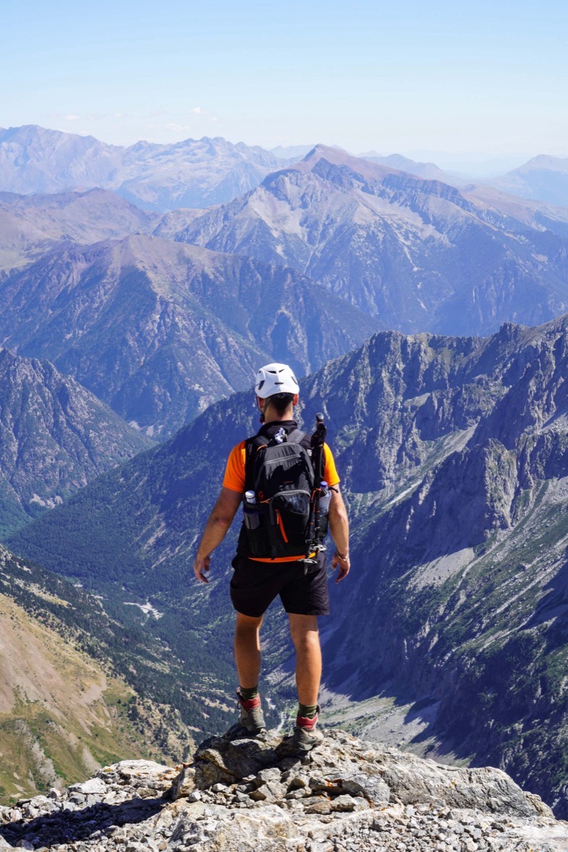 Un montañero con casco, de espaldas, sobre una roca en el filo de la cresta de La Munia. Debajo se abre el valle de Pineta, y al fondo se encadenan las sierras del Pirineo aragonés hasta perderse en la calima.