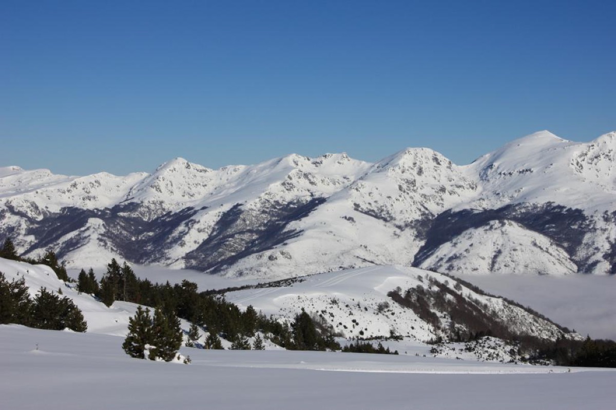 El Plateau de Beille cubierto de nieve: una extensión blanca sin apenas pendiente en primer término, algunos pinos cargados de nieve, y al fondo la cadena de cumbres nevadas del Ariège sobre un mar de nubes que llena el valle.