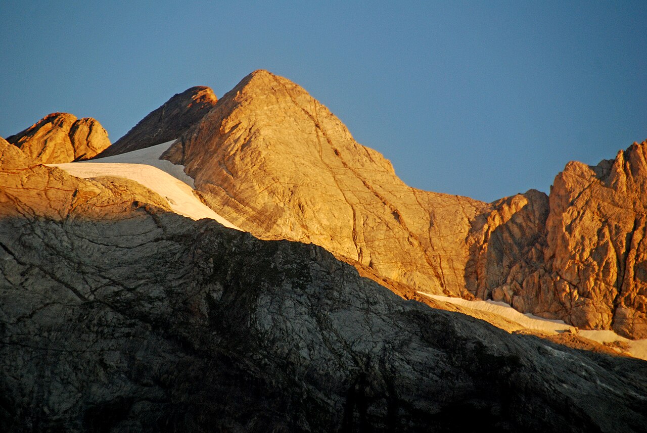 La cara del Pique Longue del Vignemale encendida por el sol naciente, roca dorada sobre un nevero blanco, con el resto del macizo todavía en sombra alrededor.